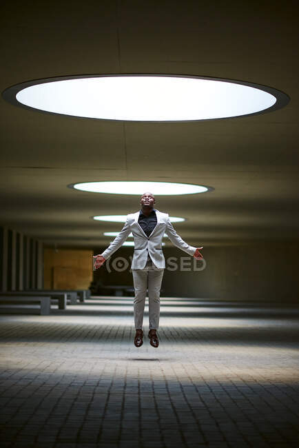 Un uomo d'affari afroamericano illuminato da un lucernario che salta. Sembra che sia stato rapito dal lucernario nel cortile.. — Foto stock