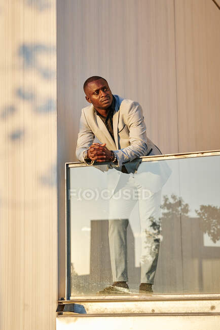 Un homme d'affaires afro-américain au coucher du soleil dans un immeuble. Il se prélasse au soleil du soir. L'ombre d'un arbre est projetée sur le mur — Photo de stock