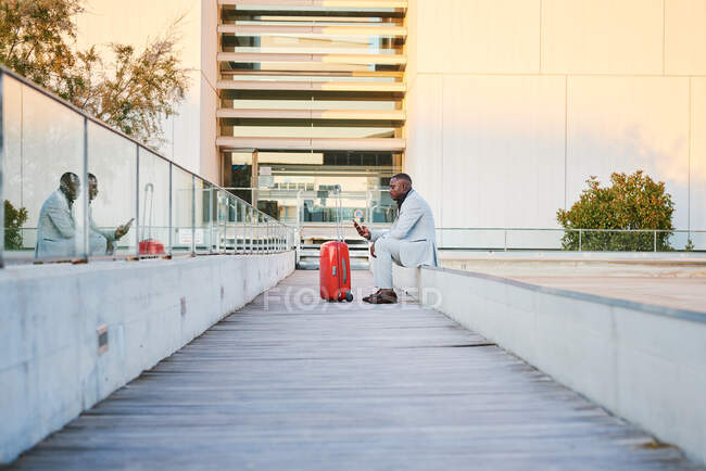 Traveler with a red suitcase and a cell phone. She's African-American and wears a fancy suit. — Stock Photo