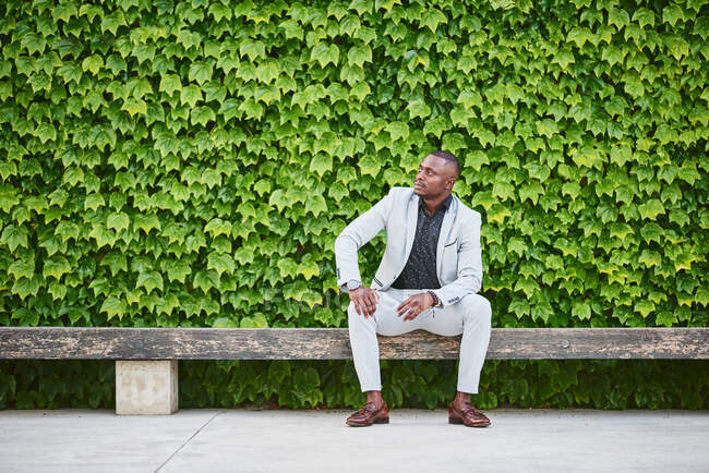 Afroamerikaner sitzt auf einer Parkbank. Er ist ein stattlicher Geschäftsmann. — Stockfoto