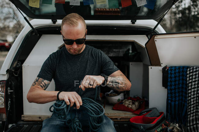 Uomo seduto sul retro del camion preparare corde per arrampicata su roccia — Foto stock