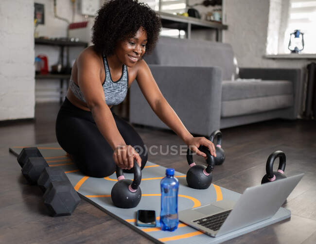 Fröhliche schwarze Frau mit Ausrüstung, die lächelt und Online-Trainingsvideo auf Laptop anschaut — Stockfoto