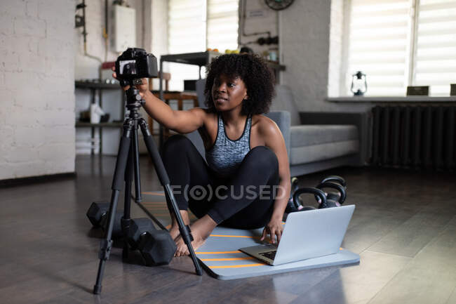 Черная женщина тренер тюнинг камеры и ноутбука перед съемкой онлайн тренировки на дому — стоковое фото