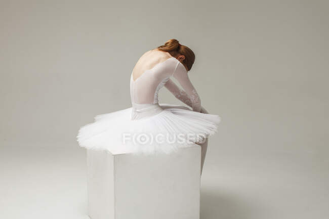 Attractive woman, ballerina in white ballet dress sitting on cube, studio shot — Stock Photo
