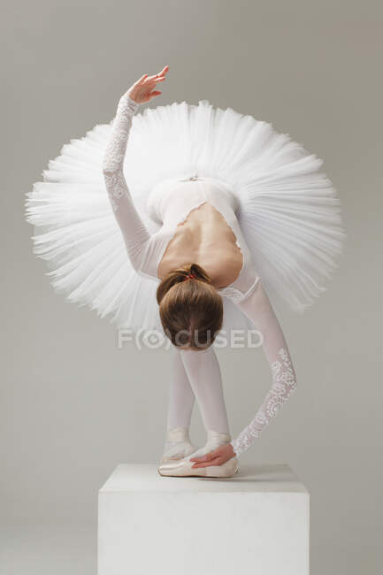 Balletttänzer in weißem Balletttutu verbeugt sich auf Sockel, isoliert auf grauem Studiohintergrund — Stockfoto