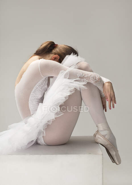 Müde Ballerina im weißen Ballettkleid sitzt auf Würfel in fetaler Position — Stockfoto