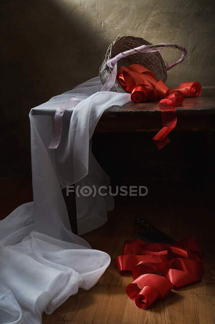 Bodegón con un paño blanco y una cesta volcada de cintas rojas - foto de stock