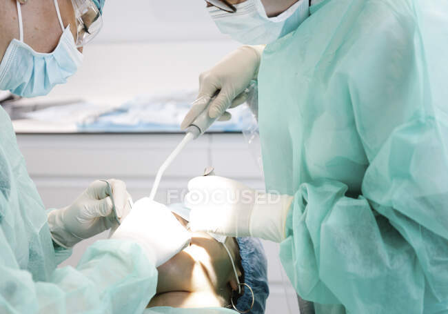 Снизу женщины-стоматологи в форме с помощью профессиональных инструментов делают операцию на анонимном пациенте во время работы в современной клинике — стоковое фото
