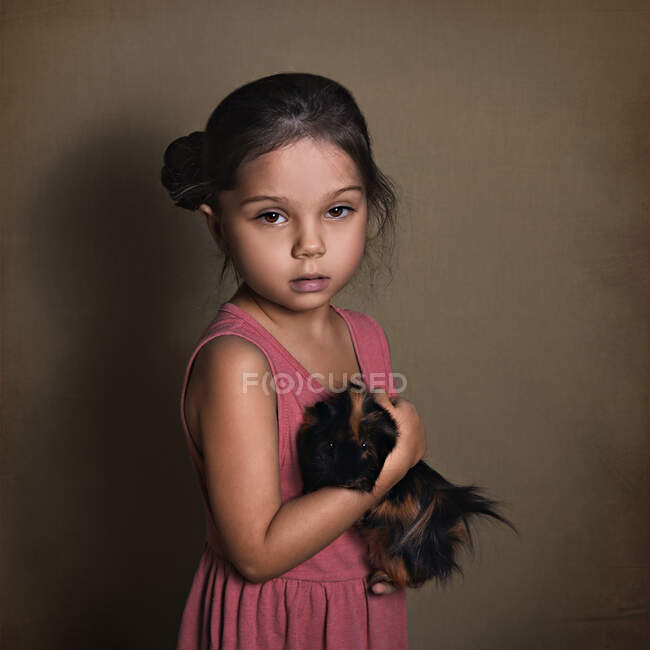 Beautiful baby girl holding a fluffy Guinea pig on a paper background — Stock Photo