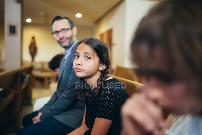 Девушка в церковной скамье с отцом рядом с ней делает глупое лицо — стоковое фото