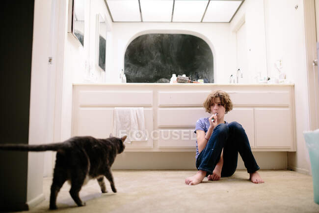 Adolescente menina preguiçosamente escova os dentes enquanto olha para o gato — Fotografia de Stock