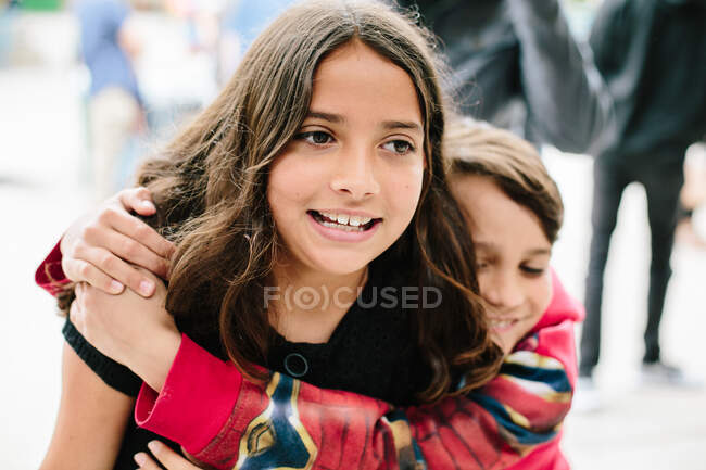 Menino felizmente abraços menina por trás enquanto ela sorri olhando oprimido — Fotografia de Stock