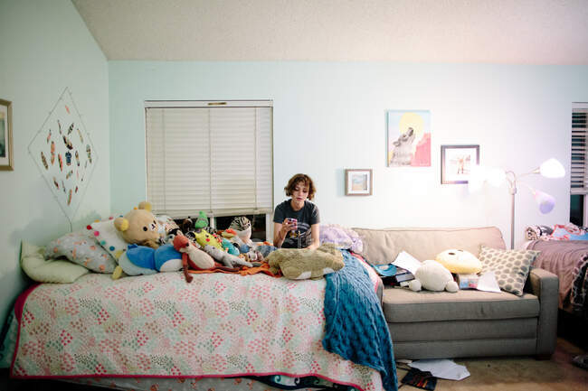 Adolescente aux cheveux courts s'assoit sur son lit en regardant son téléphone — Photo de stock