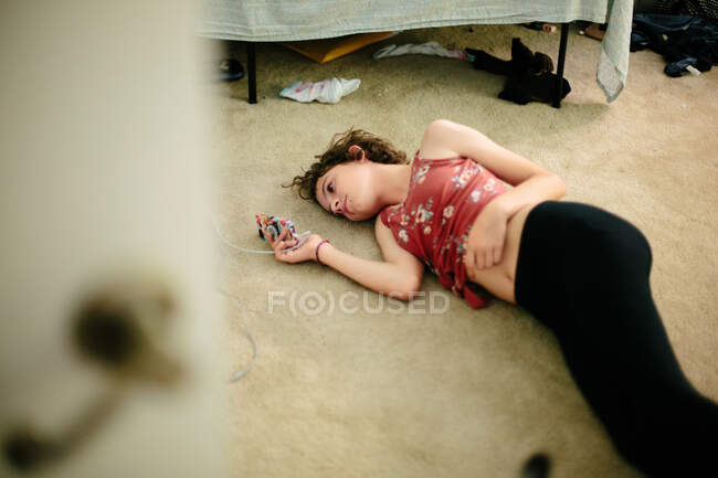 Teenie Mädchen liegt auf dem Teppichboden ihres Zimmers und schaut auf ihr Handy — Stockfoto