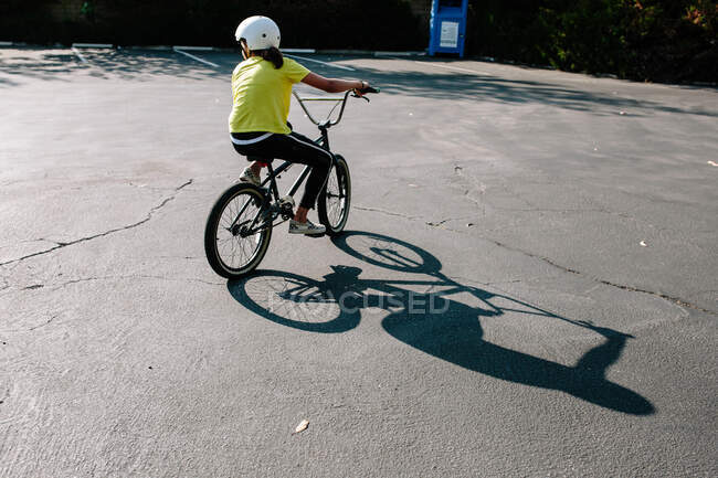 Costas de uma menina e sua sombra andando de bicicleta bmx em um estacionamento — Fotografia de Stock