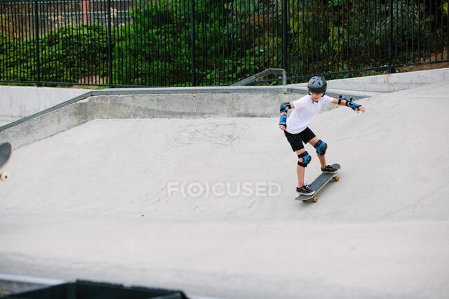 Niño monopatín en un skatepark mientras usa equipo de protección - foto de stock
