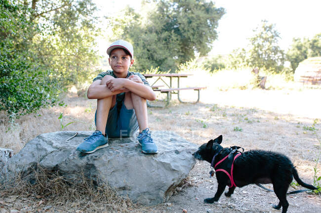 Boy sits on a large rock daydreaming with his dog nearby — Stock Photo