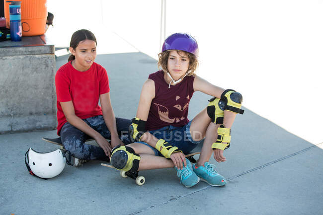 Две девушки сидят в тени со скейтбордами в скейтпарке — стоковое фото