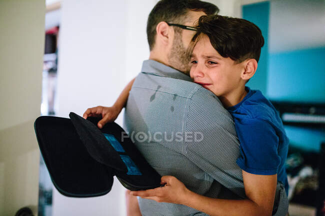 Padre sostiene hijo que está llorando mientras las lágrimas rayan la camisa de papá - foto de stock