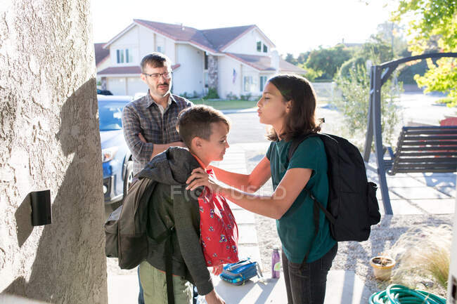 Отец присматривает за детьми снаружи, пока они готовятся идти в школу. — стоковое фото
