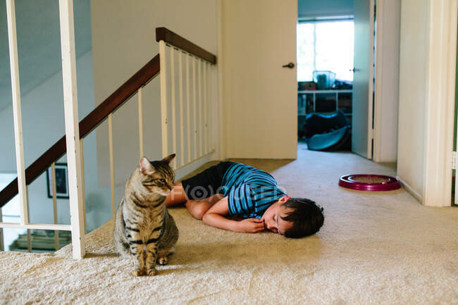 Garçon se couche sur le palier de l'escalier à côté de son chat tabby — Photo de stock