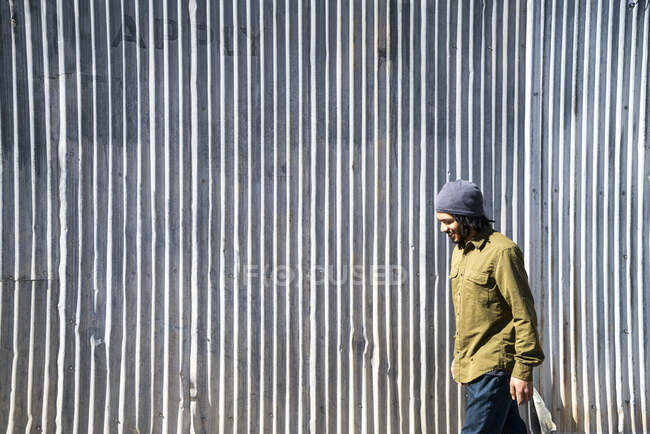 Smiling, young, African-American man walks in front of metal wall — Stock Photo