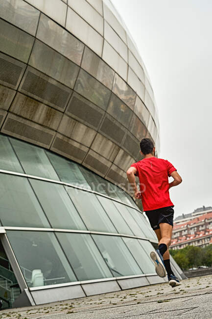 Молодий чоловік бігає в червоній сорочці і чорні штани через парк — стокове фото