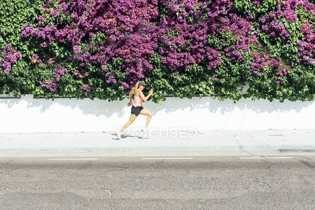 Donna che fa jogging per strada, con fiori colorati sullo sfondo — Foto stock