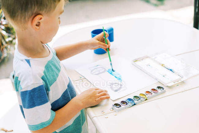 Маленький хлопчик малює машину з акварелями зовні на патіо — стокове фото