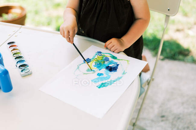 Pequena criança pintura menina com aquarelas fora no pátio — Fotografia de Stock