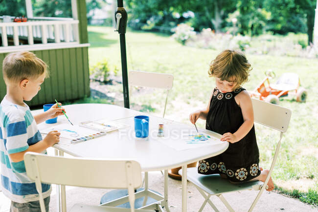 Два брата и сестра рисуют акварелью на террасе — стоковое фото