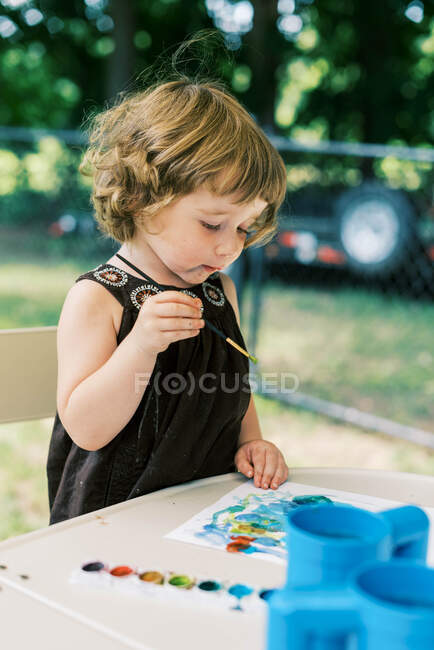 Little artist painting with watercolors outside on the patio — Stock Photo