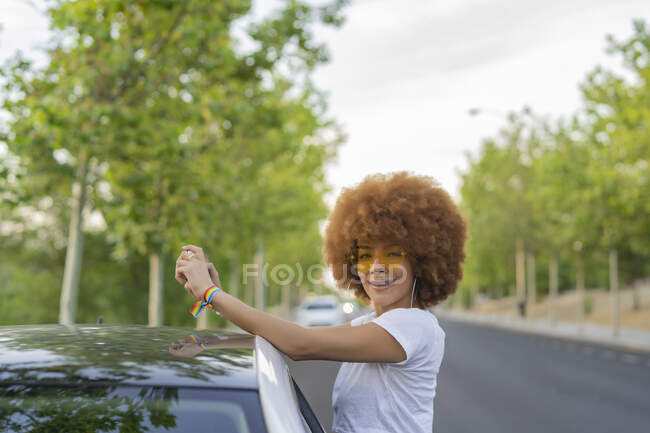 Frau mit Afrohaaren fotografiert mit ihrem Smartphone neben ihrem weißen Auto — Stockfoto
