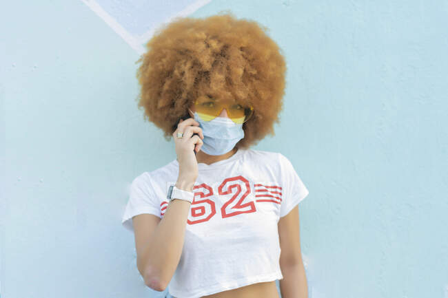 Mujer con pelo afro y mascarilla hablando en su smartphone - foto de stock
