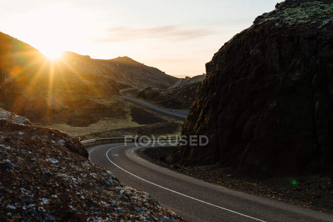 Strada asfaltata tortuosa in prossimità di formazioni rocciose grezze durante il tramonto in altopiano mozzafiato — Foto stock