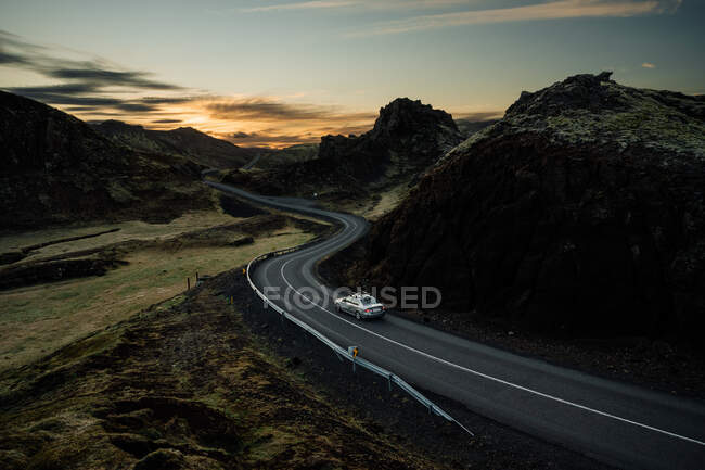 Modern vehicle driving on winding asphalt road through picturesque mountainous terrain during sunset in countryside — Stock Photo