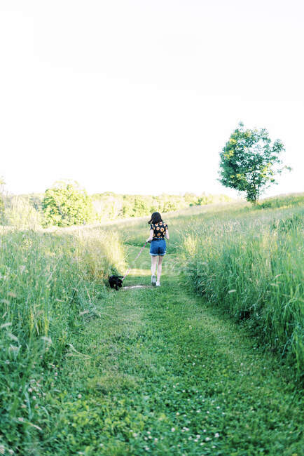 Девочка-подросток выгуливает щенка на поводке в поле — стоковое фото