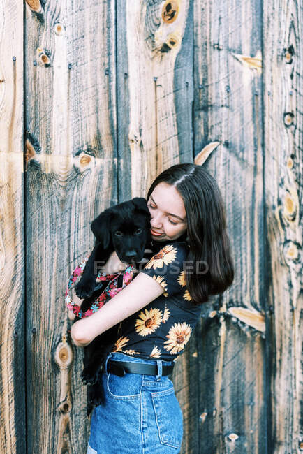 Дівчинка - підліток обіймає свого двомісячного чорного лабрадора. — стокове фото