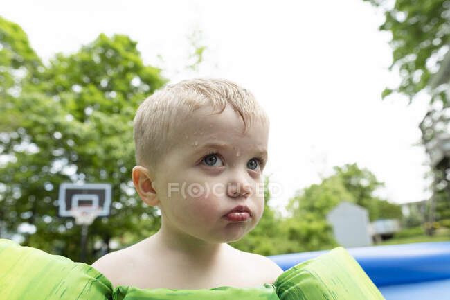 Angry child pouts next to swimming pool while water drips down face — Stock Photo