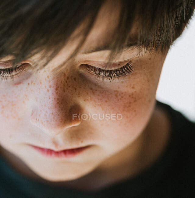 Close up of the face of a young boy with freckles looking downward. — Stock Photo