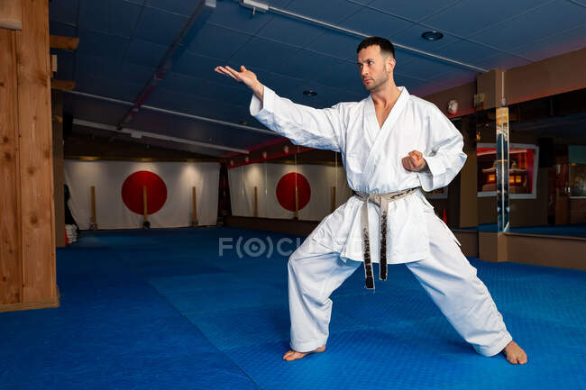 Karate hombre de pie su terreno en tatami usando kimono blanco - foto de stock