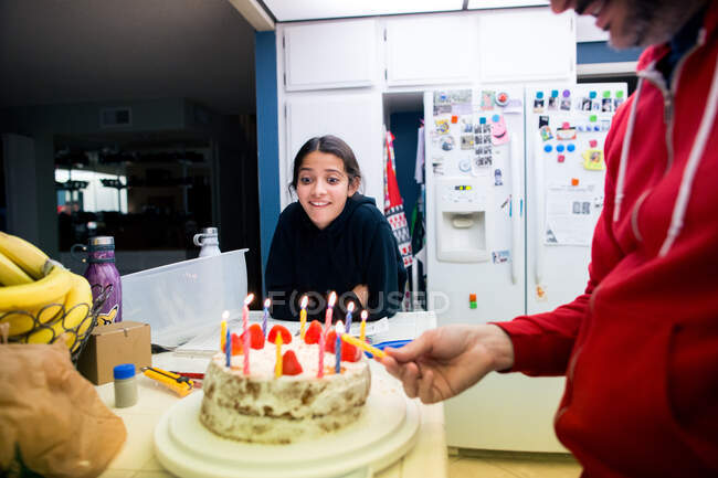 Father lights candles on daughter's cake while she looks excited — Stock Photo