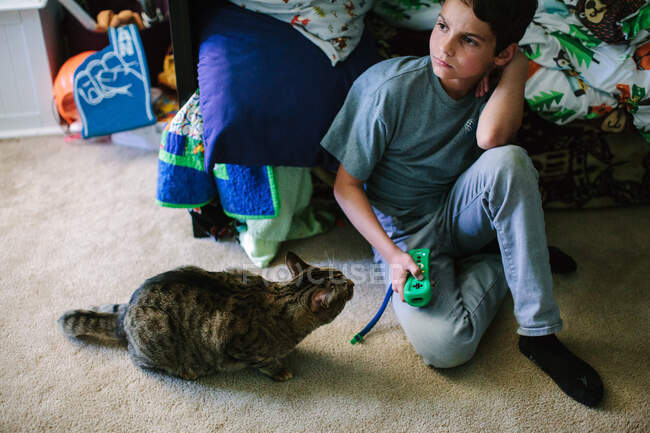 Tabby gato senta-se ao lado do menino como ele mantém seu controlador de videogame — Fotografia de Stock