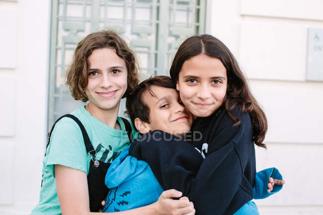 Hermanito consigue sandwiched en un abrazo por sus hermanas mayores - foto de stock