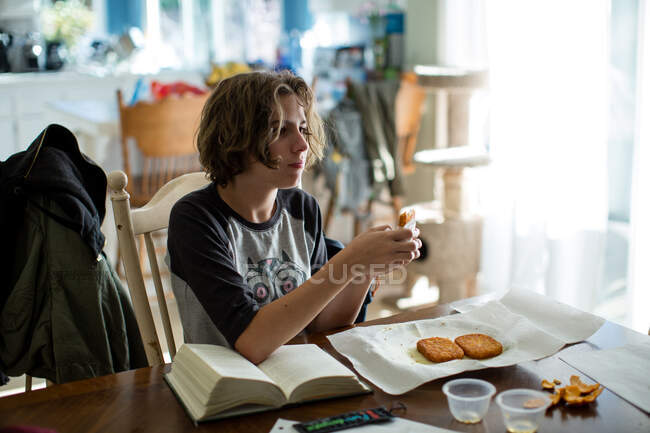 Chica de catorce años se sienta en una mesa con su libro y bocadillos fritos - foto de stock