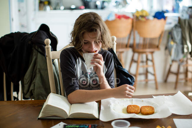 Adolescente menina dá uma mordida de um hash marrom enquanto ela lê seu livro — Fotografia de Stock