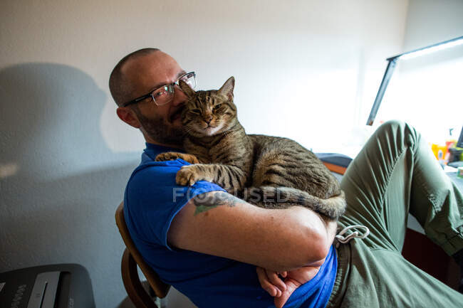 Homem com óculos segura seu gato marrom e sorri — Fotografia de Stock