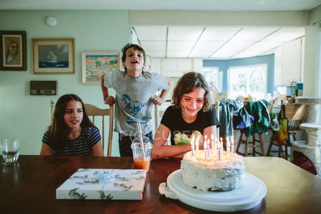 Adolescent regarde les bougies sur son gâteau tandis que les frères et sœurs chantent — Photo de stock