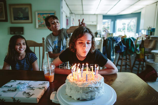 Adolescente menina apaga velas de seu bolo de aniversário com irmãos perto — Fotografia de Stock