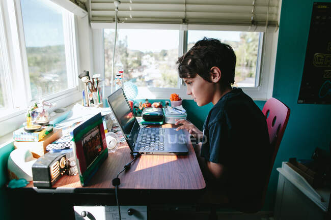 Dieci anni ragazzo prende una chiamata zoom sul suo computer portatile per homeschool — Foto stock